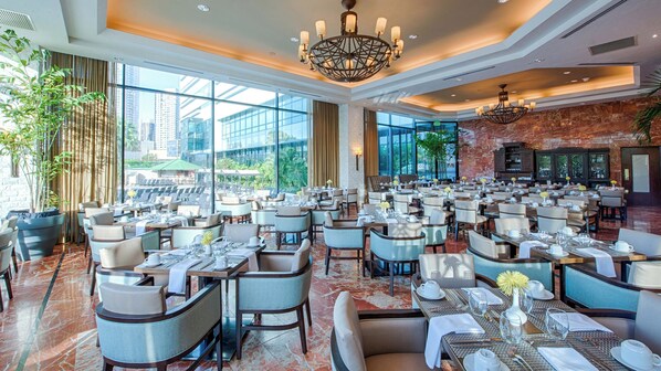 A spacious dining area with multiple tables and chairs, large windows offering a view of the city, and a chandelier hanging from the ceiling. - InterContinental Miramar Panama by IHG (Panama City)