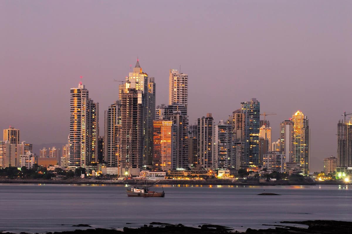 A city skyline at dusk with high-rise buildings and a body of water in the foreground.