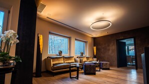 A modern living room with a sofa, coffee table, and ottoman, large windows, and a wooden floor. - Hotel Alpenrose Kufstein (Kufstein)