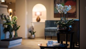 A modern living room with a coffee table, a blue armchair, and a vase with white flowers. - Hotel Alpenrose Kufstein (Kufstein)