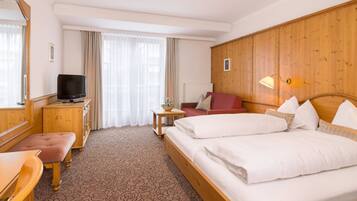 Una habitación de hotel con cabecera de madera, cama doble, escritorio con televisor, una mesita con una planta y una silla roja.