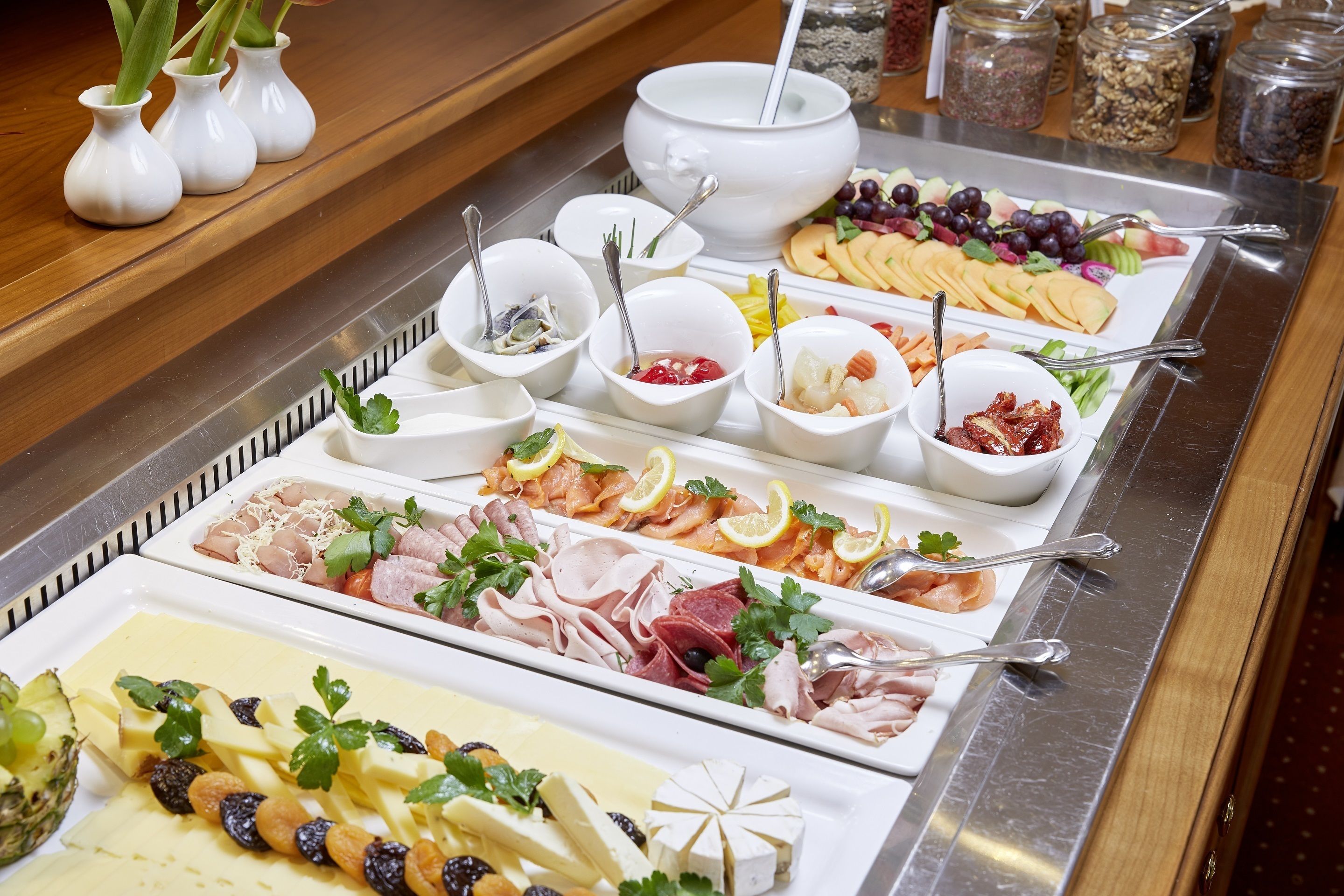 A buffet with various food items including cheeses, meats, fruits, and garnishes.