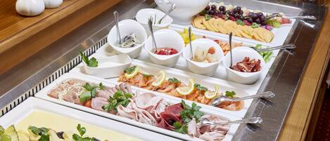 A buffet with various food items including cheeses, meats, fruits, and garnishes.