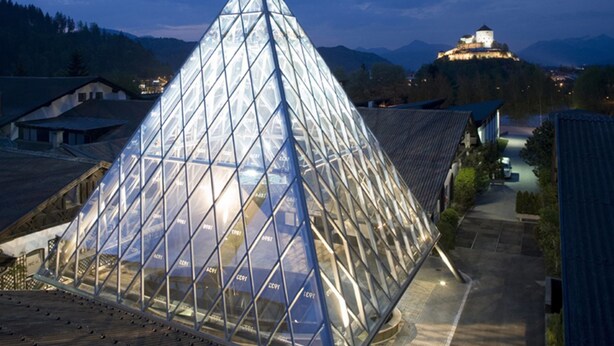 A modern glass pyramid structure with a metal framework, surrounded by traditional buildings and a mountain backdrop. - Hotel Alpenrose Kufstein (Kufstein)
