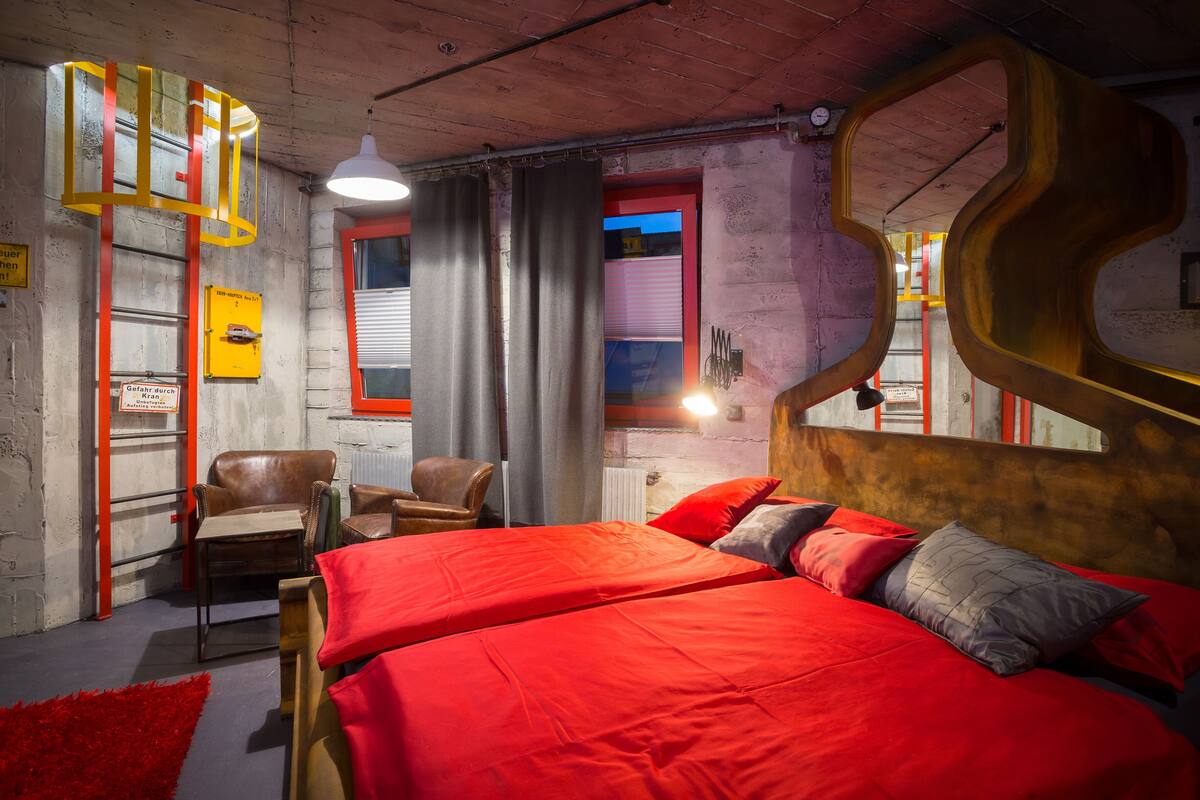 A room with a large bed, a chair, and a window with curtains.