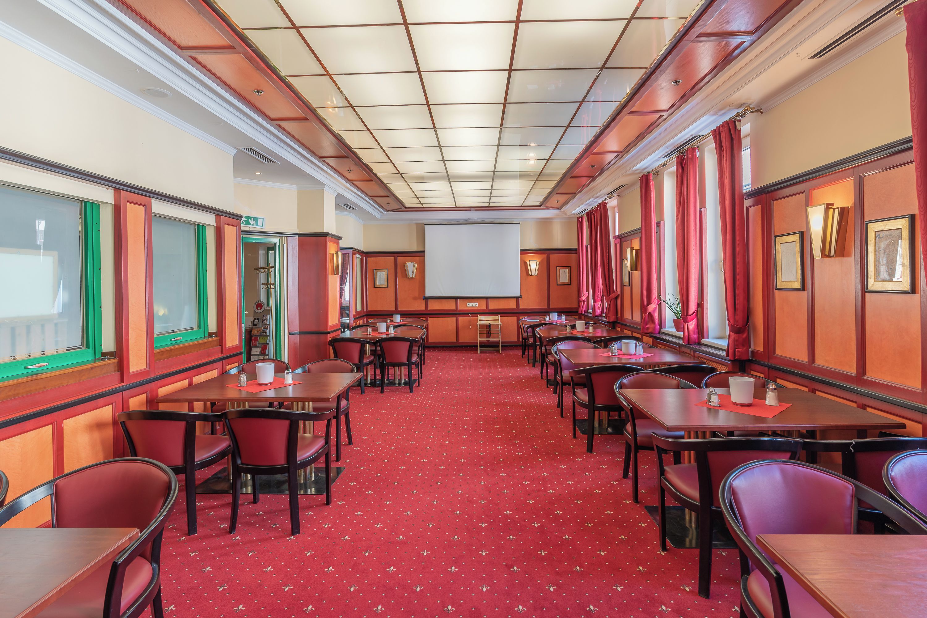 A conference room with a red carpet, wooden panel walls, and a large screen at the front.