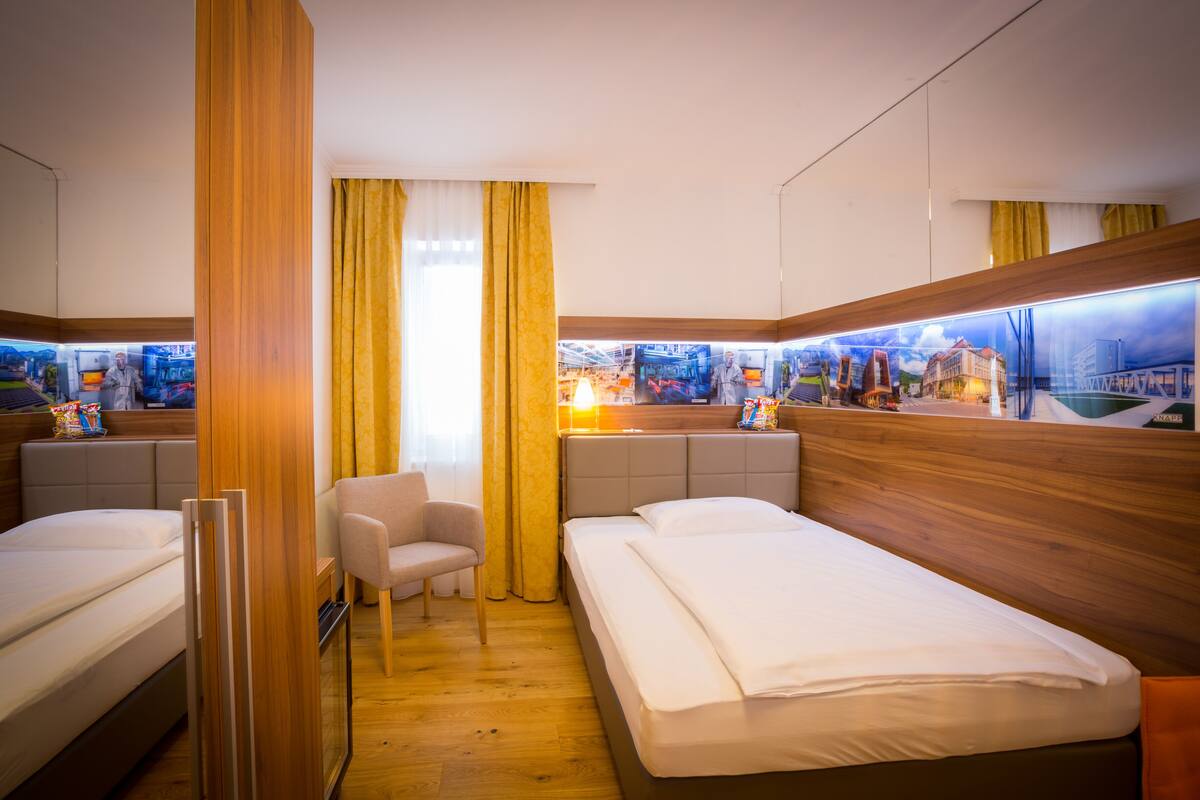 A hotel room with two beds, a chair, and a large window with curtains.