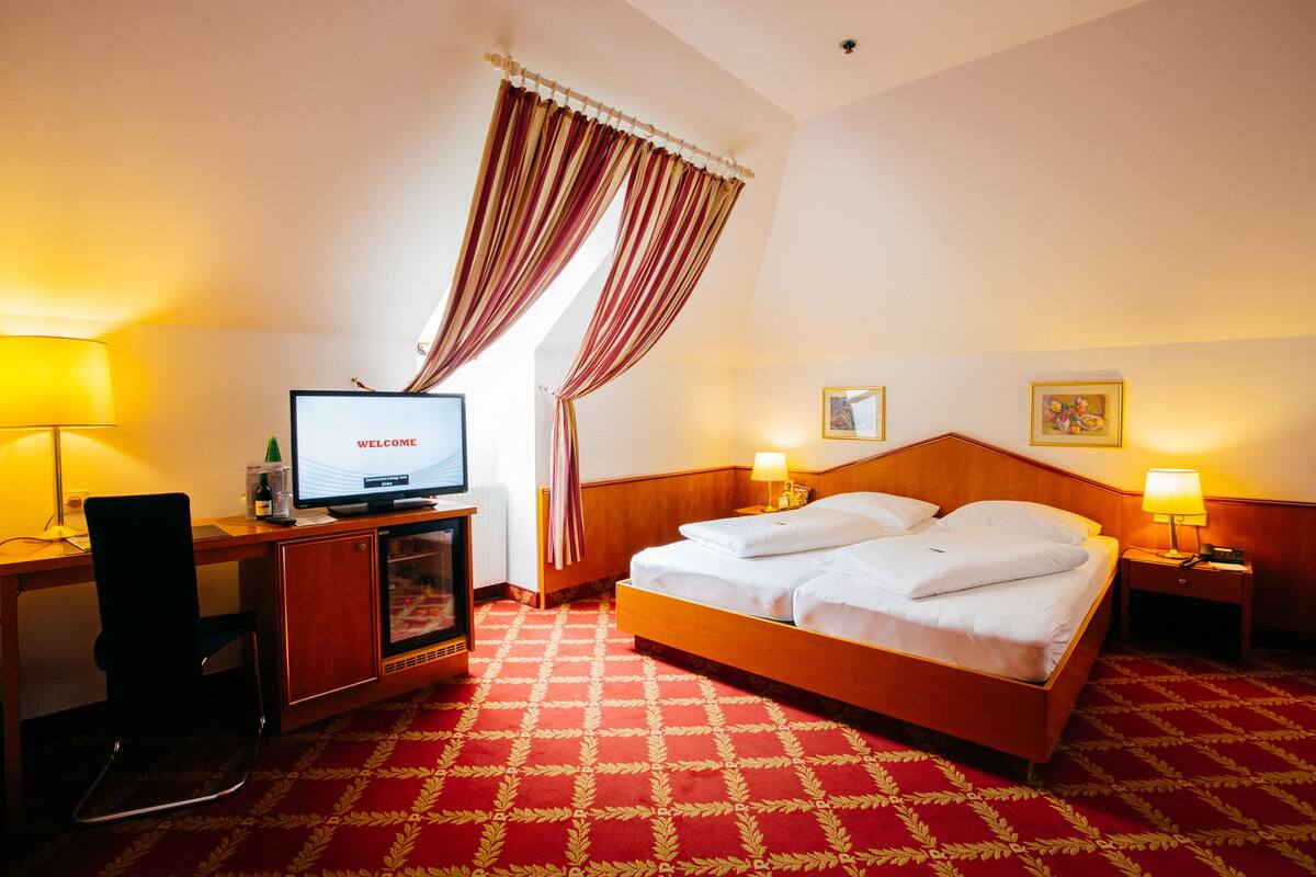 A hotel room with a bed, a desk with a computer, a TV, and two bedside lamps.