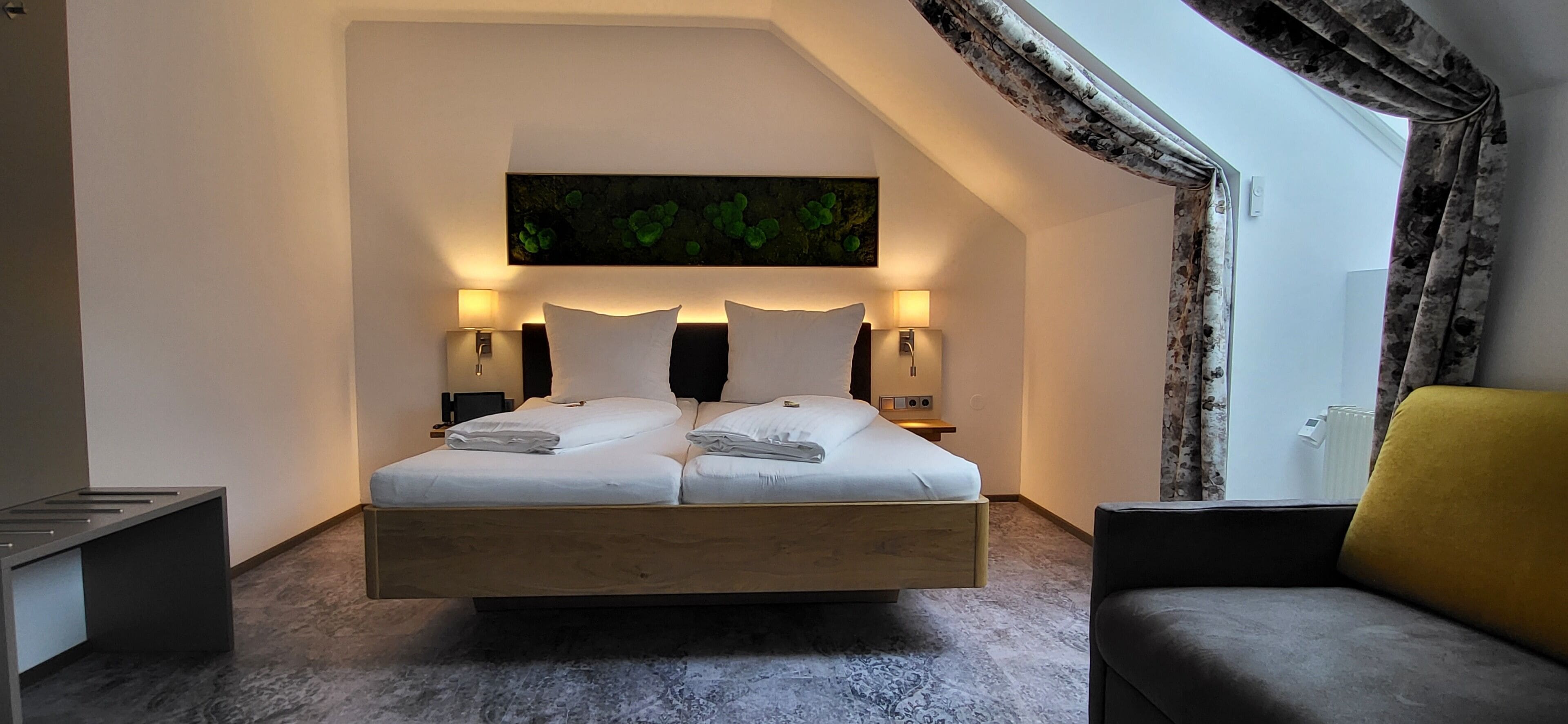 Un dormitorio moderno con una cama grande, dos lámparas de noche, un cuadro sobre la cama y vistas al exterior a través de una ventana con cortinas.