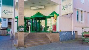 A hotel entrance with a green facade, a set of stairs leading up to the entrance, and a sign above the door. - Kongress Hotel (Leoben)