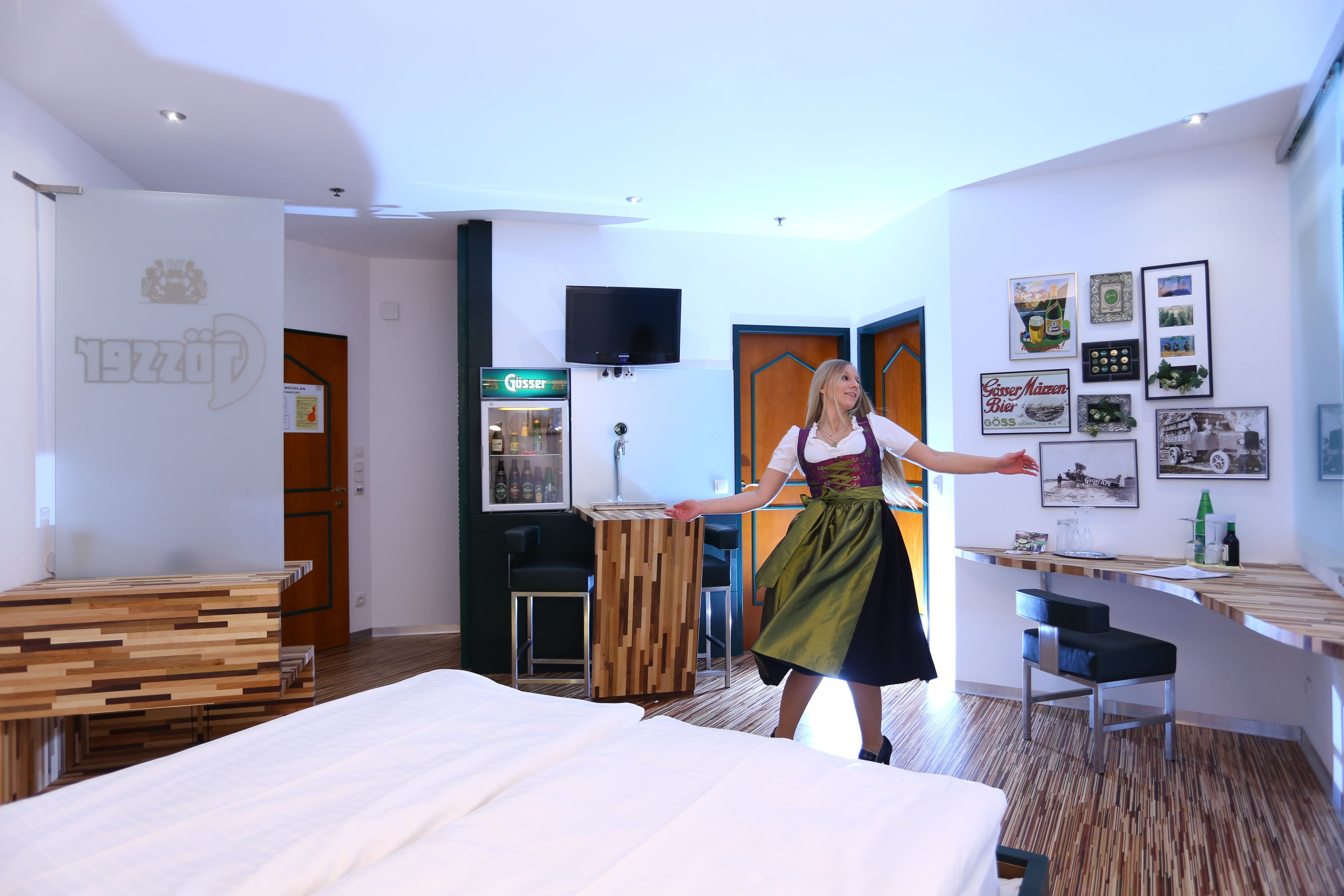 A hotel room with a bed, a wooden desk, a TV, and a wall with framed pictures.