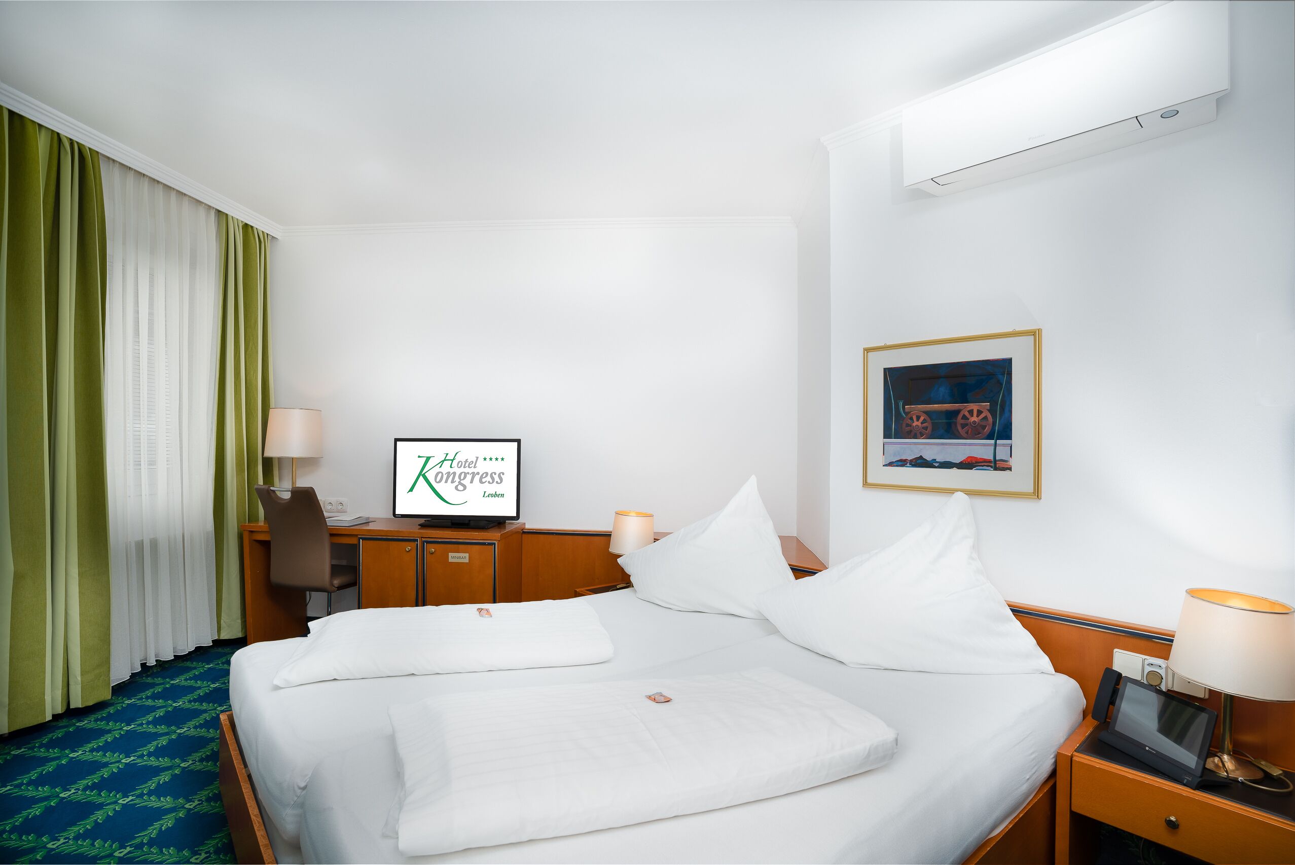 A hotel room with a bed, a desk, a chair, a TV, and a painting on the wall.
