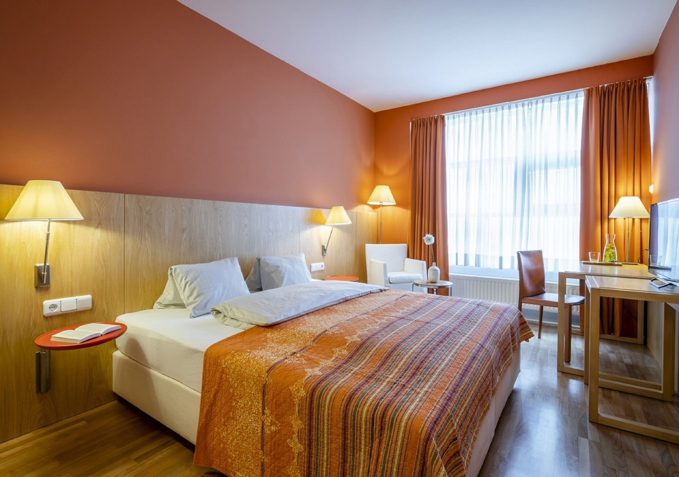 A hotel room with a bed, bedside tables, a desk, and a chair.