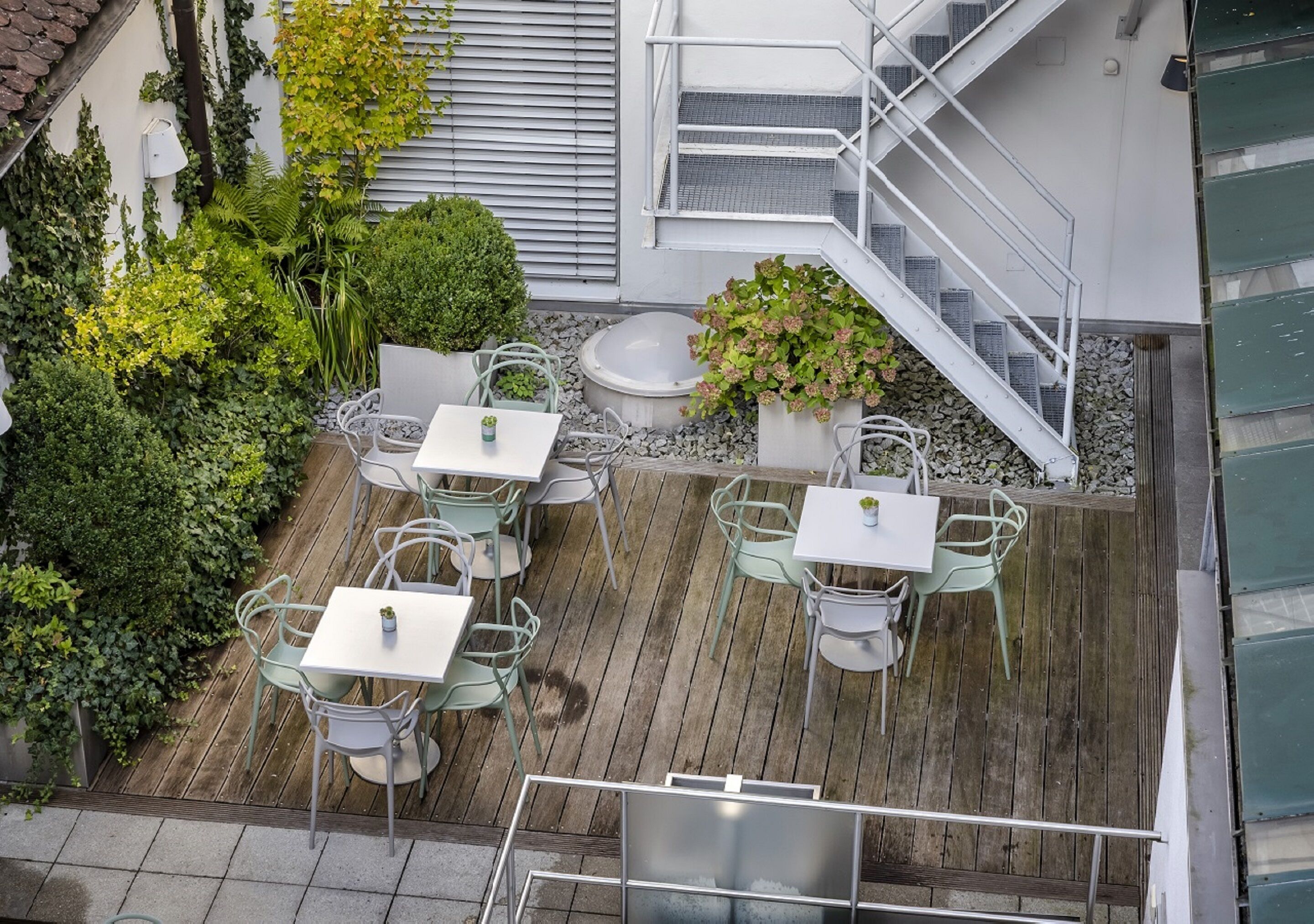 An outdoor patio with multiple tables and chairs, surrounded by lush greenery and a wooden deck.