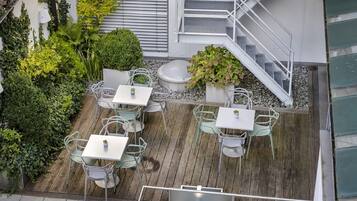 An outdoor patio with multiple tables and chairs, surrounded by lush greenery and a wooden deck.