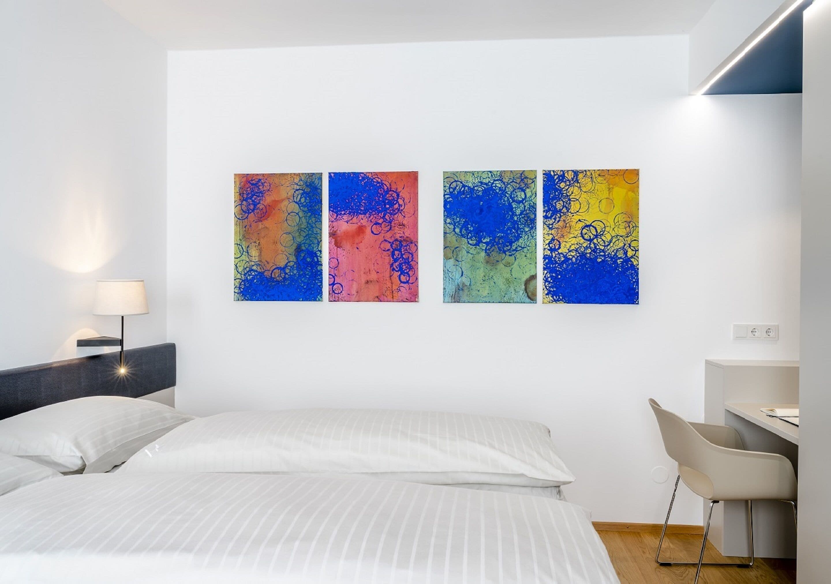 Een moderne hotelkamer met een bed, een bureau en een abstract schilderij aan de muur.