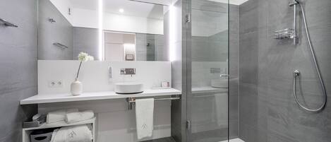 A modern bathroom with a glass-enclosed shower, a white vanity with a mirror, and a vase with flowers.