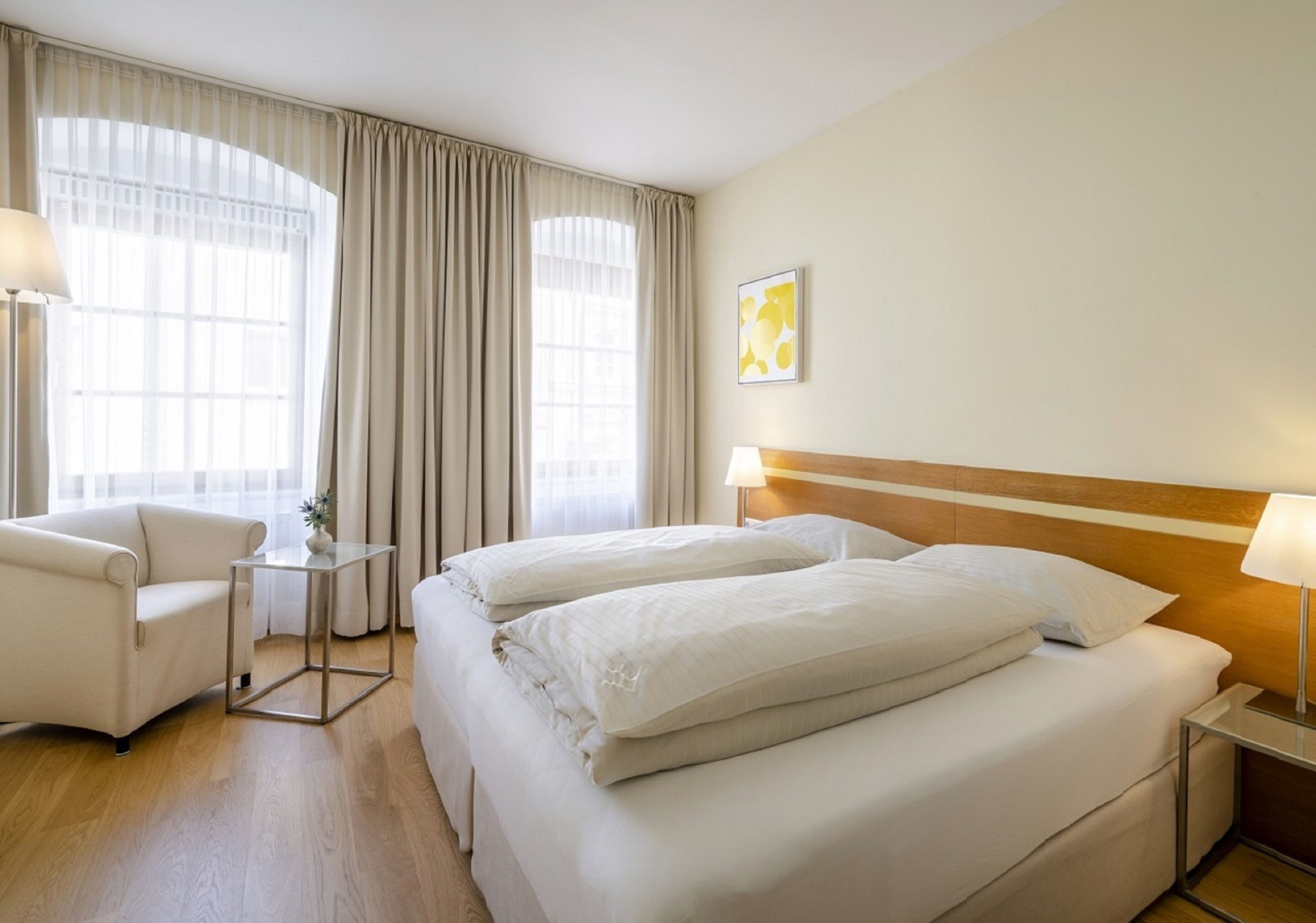 A hotel room with two beds, a chair, a small table, and a lamp.