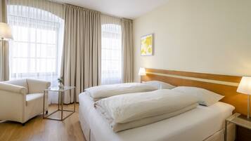 A hotel room with two beds, a chair, a small table, and a lamp.