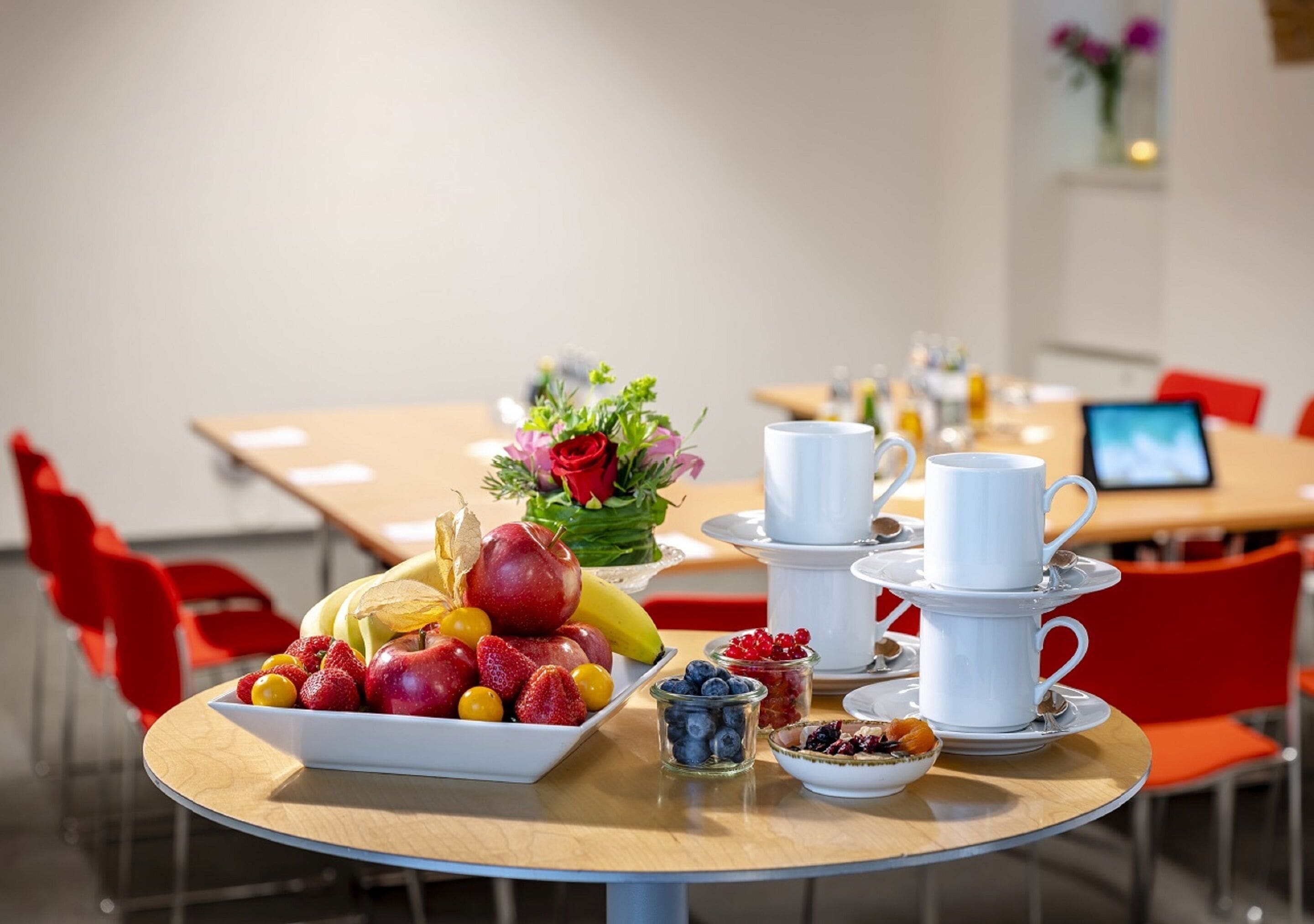 Una tavola per la colazione con frutta, tazze di caffè e un bouquet di fiori.