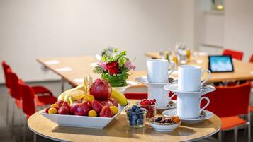 Una tavola per la colazione con frutta, tazze di caffè e un bouquet di fiori.