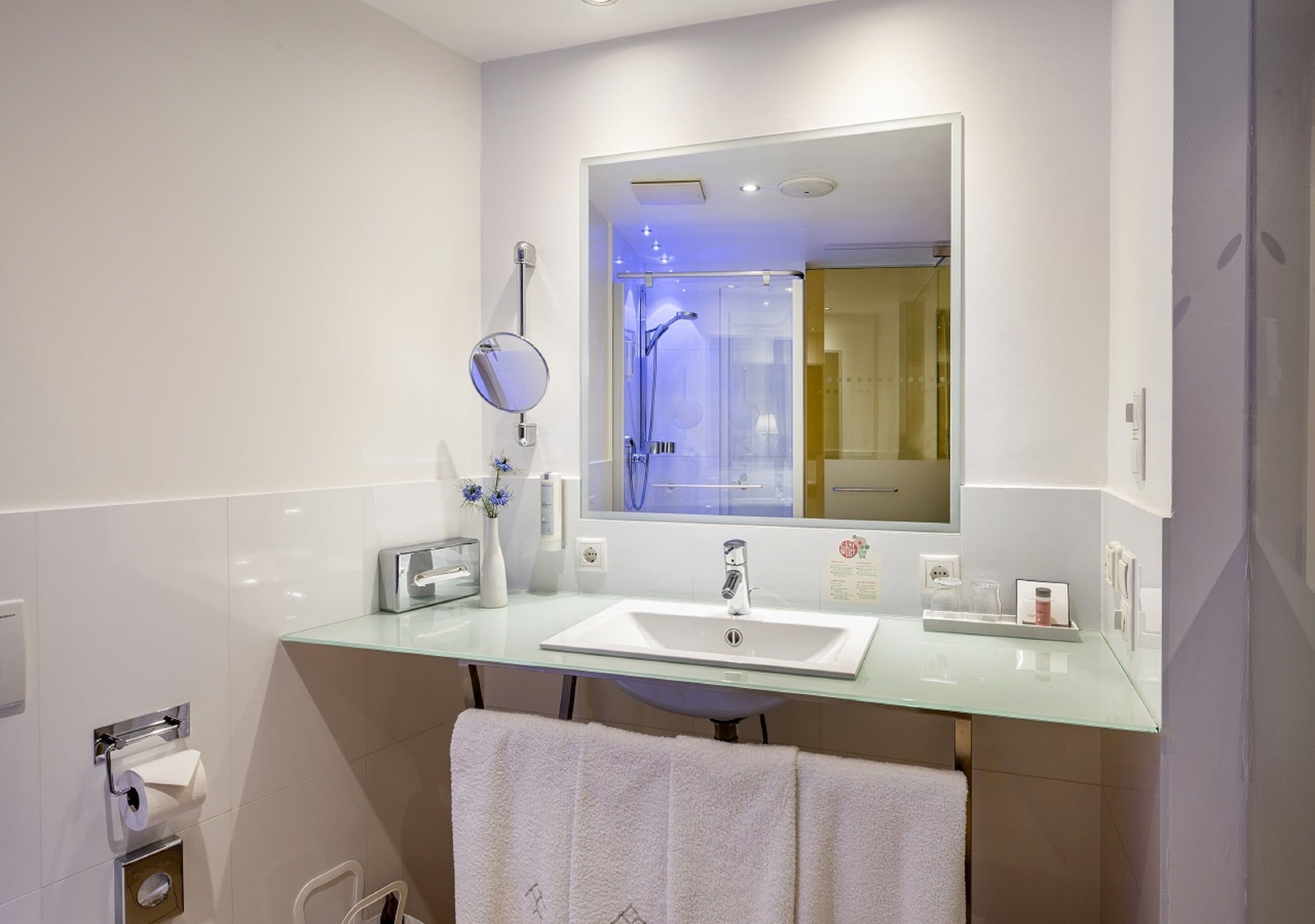 A modern bathroom with a glass sink, a large mirror, and a shower area.