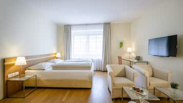 Ett hotellrum med en säng, två sängbord med lampor, en soffa, en tv och ett fönster med gardiner.