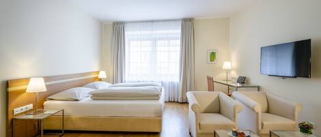 A hotel room with a bed, two bedside tables with lamps, a sofa, a TV, and a window with curtains.