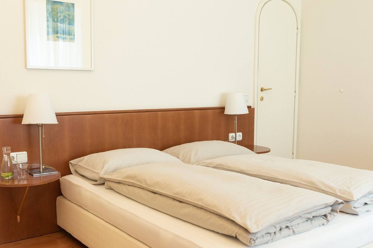 A double bed with a wooden headboard, two bedside tables with lamps, and a painting on the wall.