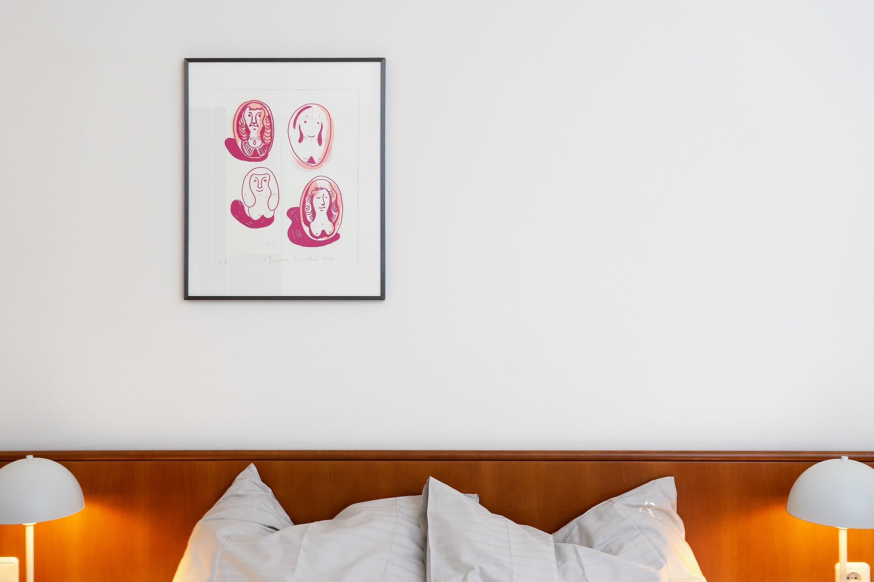 Een hotelkamer met een kunstwerk boven het bed, een houten hoofdeinde en twee bedlampen.