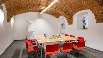 A conference room with a brick ceiling, white walls, and red chairs.