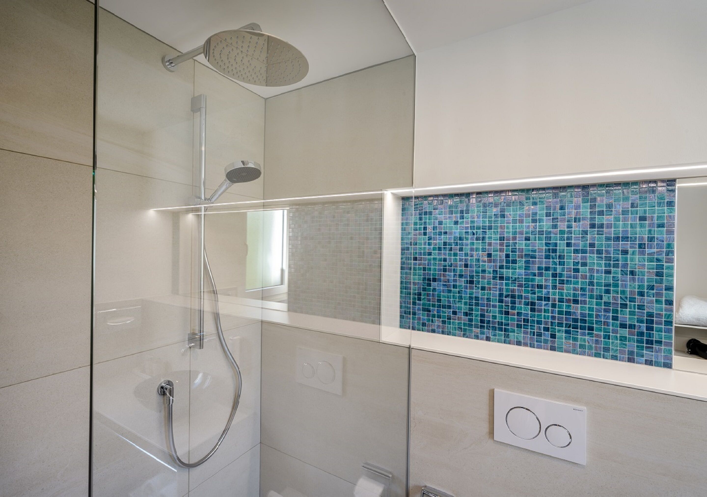 Un baño moderno con ducha envuelta en vidrio, pared con diseño de mosaico y encimera blanca.