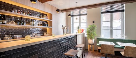 A bar area with shelves of bottles and glasses, a wooden bar counter, and a seating area with a bench and stools.