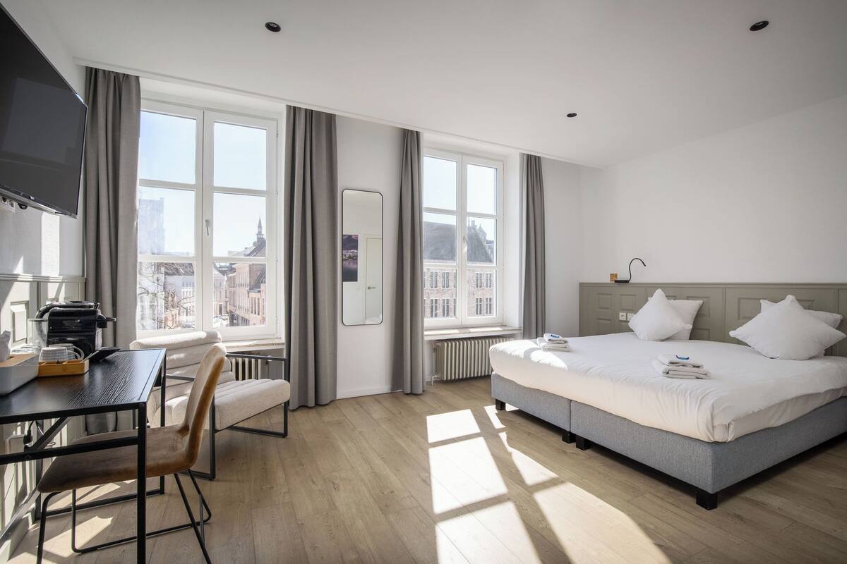 A hotel room with a bed, a desk, a chair, and a large window with curtains.