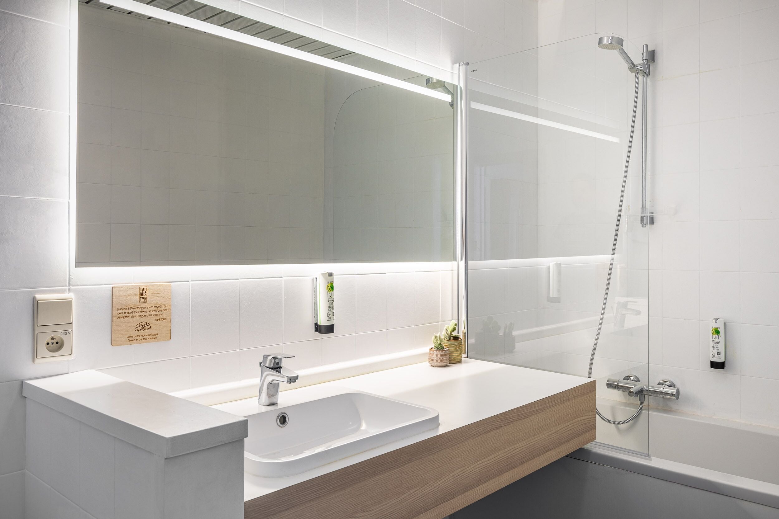 A modern bathroom with a large mirror, a sink, a shower, and a wooden vanity.