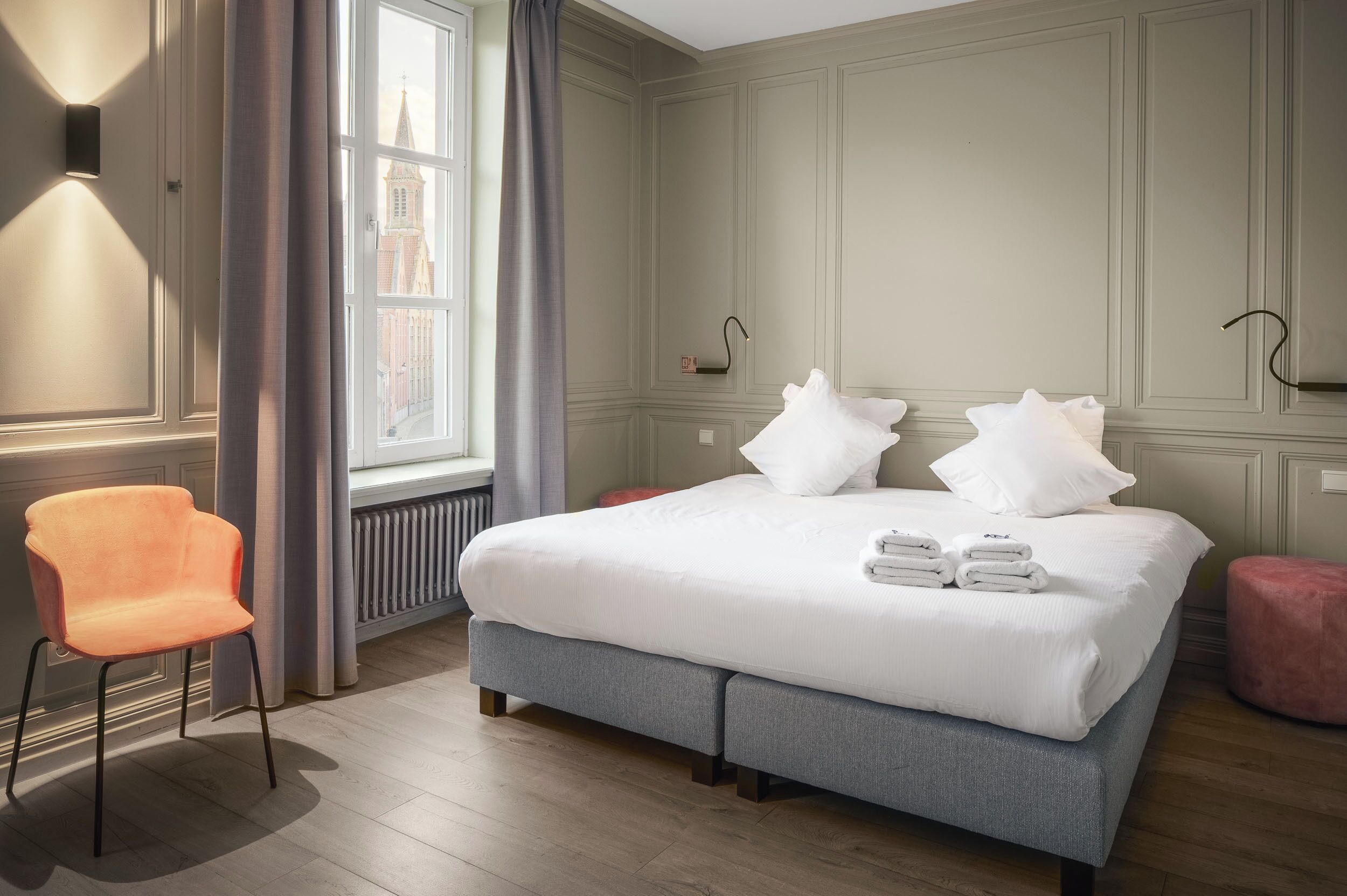 A hotel room with a bed, a chair, a window, and a radiator.