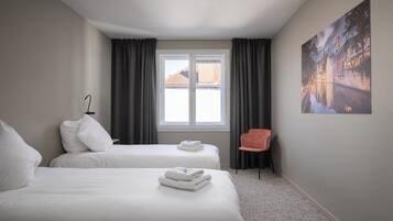 A hotel room with two beds, a window with curtains, a chair, and a painting on the wall.