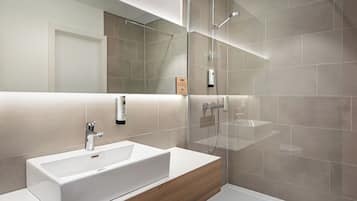 Een moderne badkamer met een grote spiegel, een witte wastafel, een douchecabine en een houten wastafelmeubel.