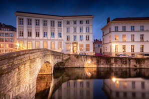 A stone bridge over a calm water body with buildings on either side, including a prominent white building with the name "AUGUSTYN" on its facade. - Hotel Augustyn (Bruges)