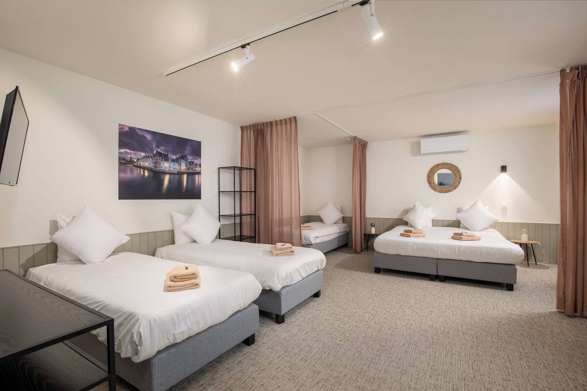 A hotel room with two single beds, a double bed, a desk, and a large window.