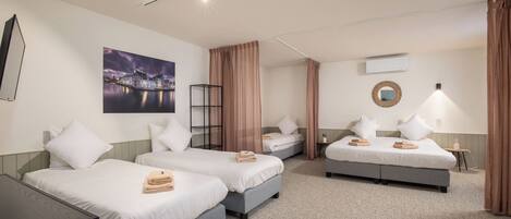A hotel room with two single beds, a double bed, a desk, and a large window.