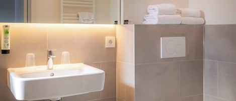 A modern bathroom with a sink, mirror, towel rack, and toilet.