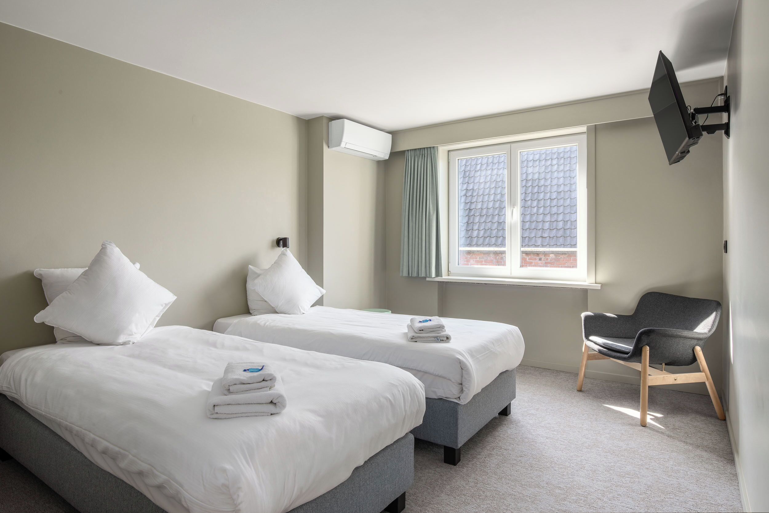 A hotel room with two beds, a flat-screen TV, a window with curtains, and a chair.