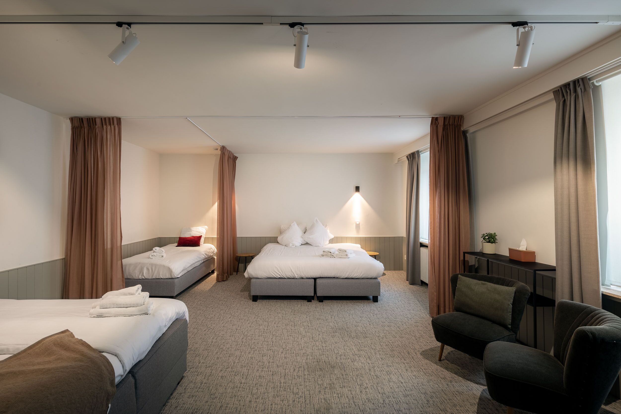 A hotel room with two beds, a sofa, a desk, and a large window with curtains.