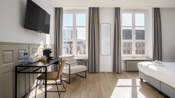 Una habitación de hotel con cama, escritorio con silla, televisor y ventana con cortinas.
