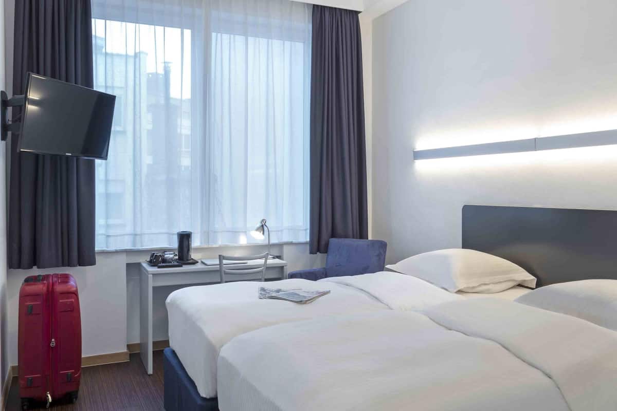 Una habitación de hotel con una cama grande, un escritorio, un televisor y una maleta.
