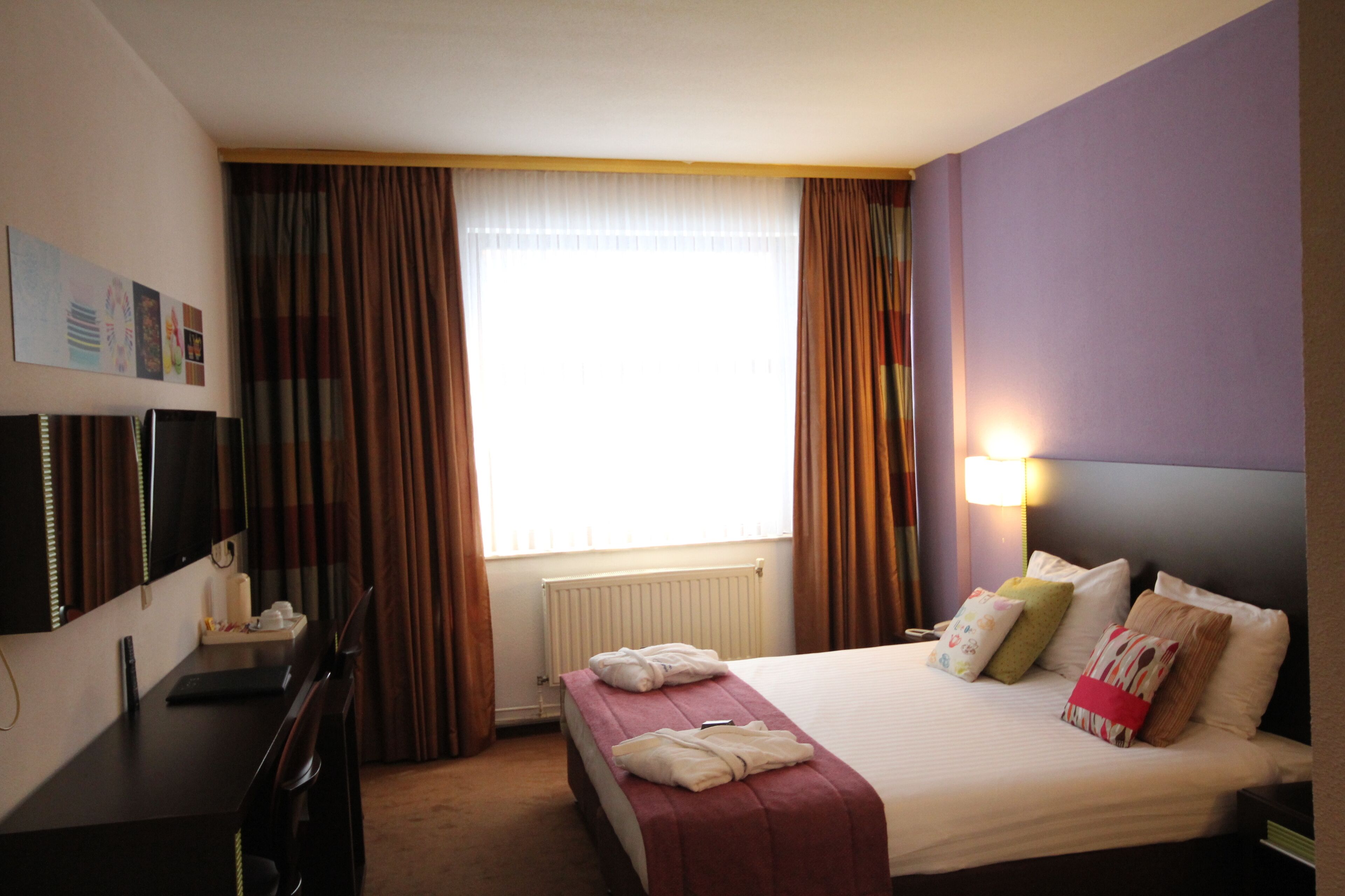 Een hotelkamer met een bed, een bureau, een stoel, een televisie en een raam met gordijnen.