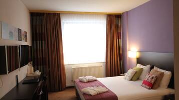 Een hotelkamer met een bed, een bureau, een stoel, een televisie en een raam met gordijnen.