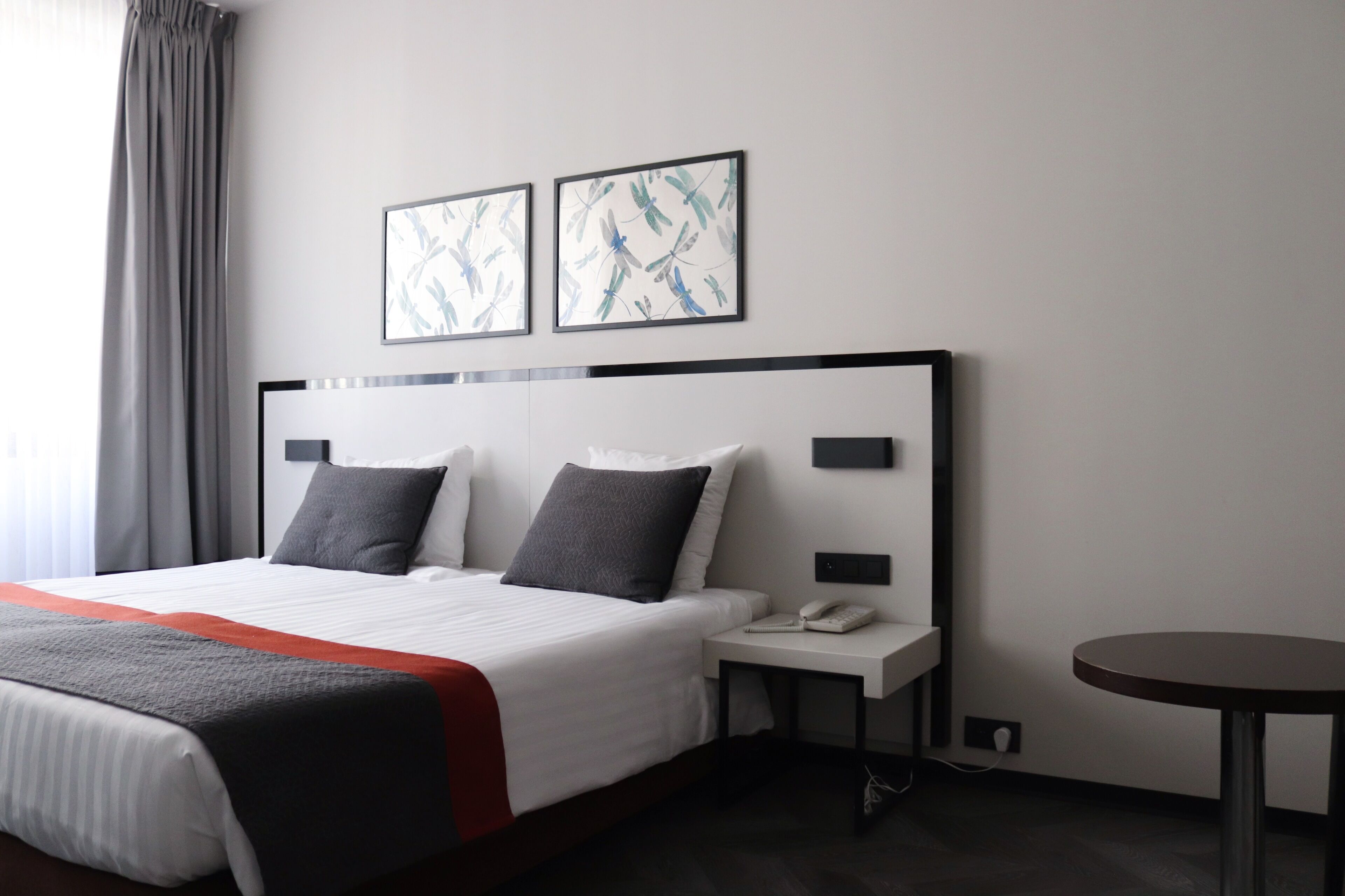 Habitación de hotel con una cama grande, dos almohadas, una mesita de noche con un teléfono y dos cuadros enmarcados en la pared.