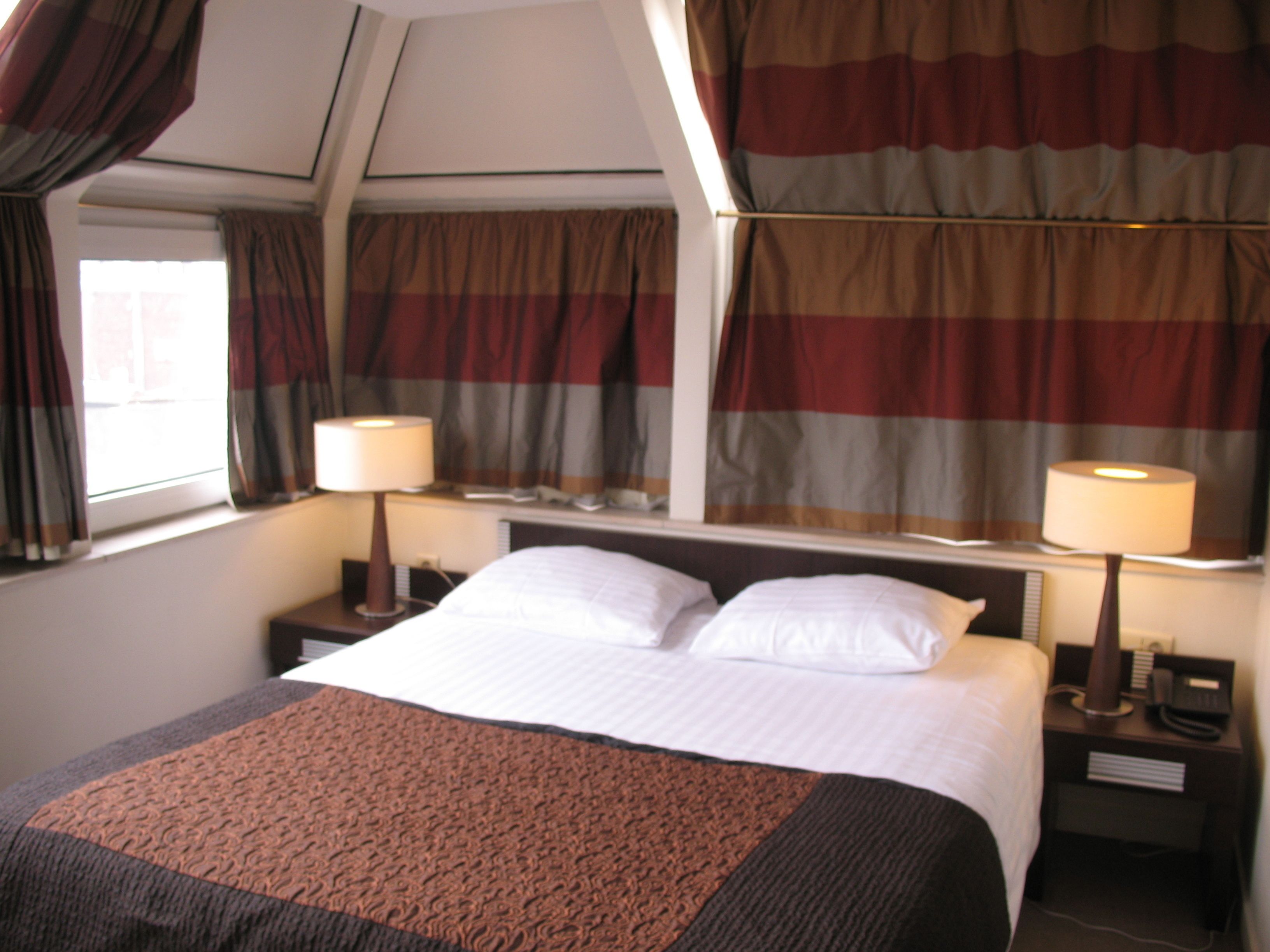 A hotel room with a large bed, two bedside tables with lamps, and curtains.